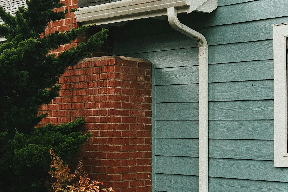 White rain gutter and downspout on a home with blue lap siding